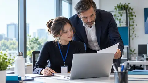 Étudiante en stage devant son ordinateur, un collègue lui présente un document